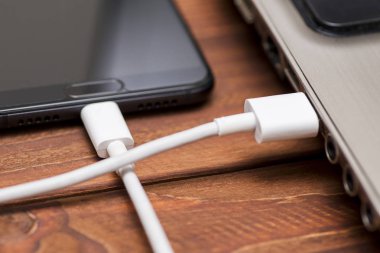 Cep telefonu laptop bağlı. Bir USB kablosu ahşap masada telefon ve dizüstü bilgisayar bağlanır. Dizüstü bilgisayara bağlanan akıllı telefon