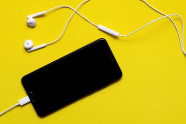 Renk arka planda kulaklıklar ile Smartphone. Sarı arka planda kulaklıklarla akıllı telefonun yakın çekim. Müzik dinleme