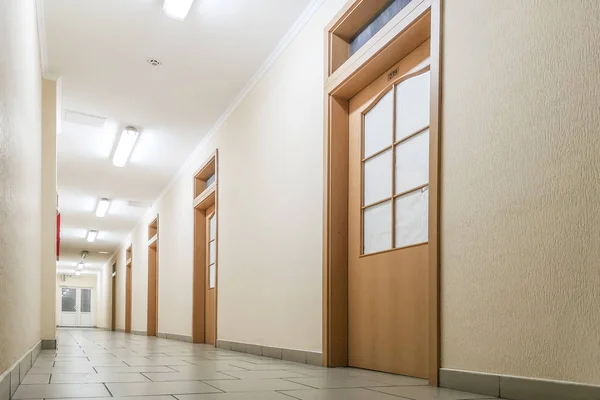 Um longo corredor vazio. Corredor de escritório vazio com muitas portas de madeira clara — Fotografia de Stock