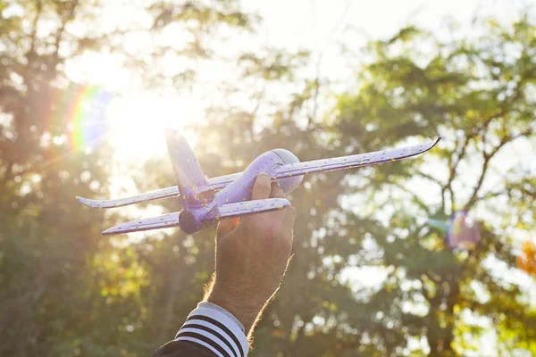 Close up photo of man\'s hand holding toy airplane against blue sky. Airplane model in hand on sunny sky. Concepts of travel, transportation, transport, dreaming about holidays