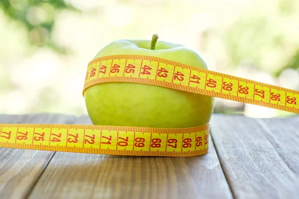 Manzana verde con cinta métrica sobre fondo de madera. Las manzanas y la cinta de coser miden en una mesa de madera. Para perder peso y comer una manzana baja en calorías para perder peso — Foto de Stock