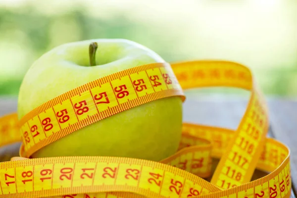 Grönt äpple med måttband på trä bakgrund. Äpplen och sömnad måttband på ett träbord. Att gå ner i vikt och äter en låg kalori apple för att gå ner i vikt — Stockfoto