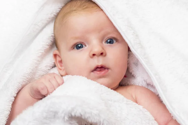 Feliz bebé con una toalla después de la ducha en la cama en casa. Un recién nacido bañado en una toalla blanca — Foto de Stock