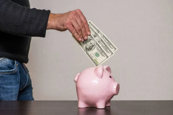 Mano masculina poniendo un billete de 100 dólares en una alcancía. Ahorrar concepto de dinero — Foto de Stock