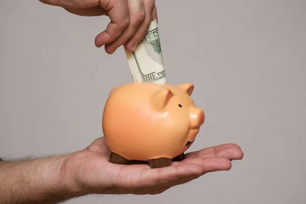 Mano masculina poniendo un billete de 100 dólares en una alcancía. Ahorrar concepto de dinero — Foto de Stock