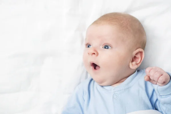 Profile portrait of cute little baby boy lying on white blanket and looking aside. Child with open mouth and wide opened eyes. Astonished surprised kid. Copyspace — Stock Photo, Image