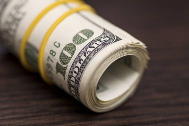 Ahşap arka plan üzerinde izole sarı bir lastik bant tarafından örülmüş yüz dolarlık banknotlar büyük bir rulo. Ahşap bir masa üzerinde yüz dolarlık banknot rulo