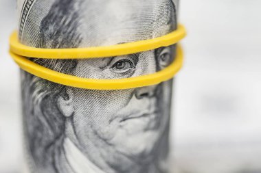 Rulo 100 dolarlık banknotlar, kauçuk bant ile Franklin'in gözleri üzerinde bir vurgu ile