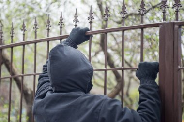 Gloved hands on fence closeup. Male thief an with hands in gloves trying to climb up a metal fence clipart