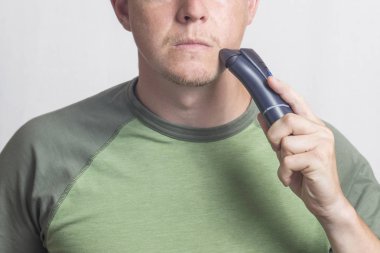 Adam tıraş ediyor. Elektrikli tıraş ve ışık arka plan ile yüzünü tıraş genç adam