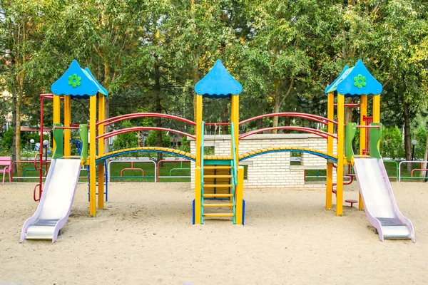 Kleurrijke kinderen speeltuin activiteiten in openbaar park omgeven door groene bomen — Stockfoto
