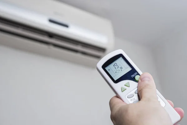 Hand with remote control directed on the conditioner on the wall. Air conditioner with remote controller