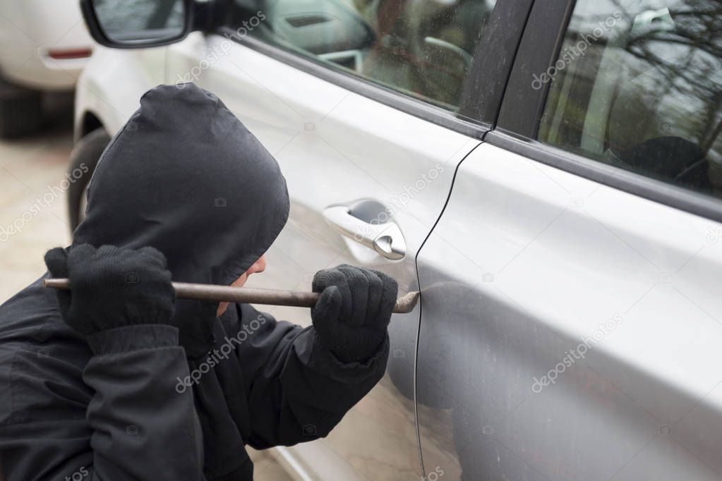 A robber dressed in black holding crowbar at a driver in a car. Car thief, car theft concept