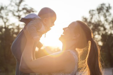 Mutlu anne gün batımında tatlı bebeğini kucağında tutuyor. Güneş batarken çocuğunu büyüten bir annenin arka plan gölgesi.