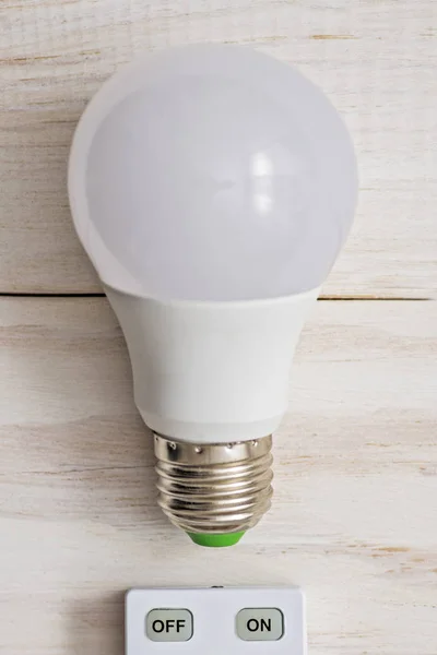 LED light bulb and remote control with buttons on and off on a white wooden background