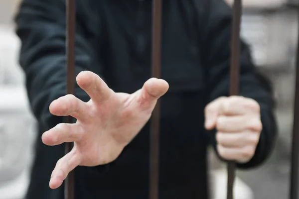 Man\'s hand stretches through the bars locked man in a cage cell. Hand of a refugee behind fence