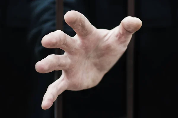 Adamın eli, bir kafes hücresine kilitlenmiş bir adamı parmaklıklar boyunca uzatır. Çitin arkasında bir mültecinin eli — Stok fotoğraf