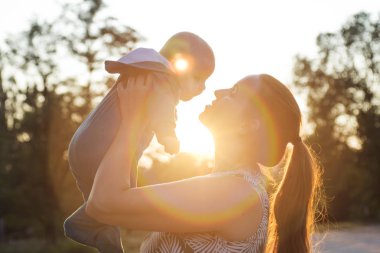 Gün batımında oğlunu büyüten bir annenin gölgesi. Ortasında güneş var. Mutlu anne gün batımında bebeğini kucağında tutuyor.