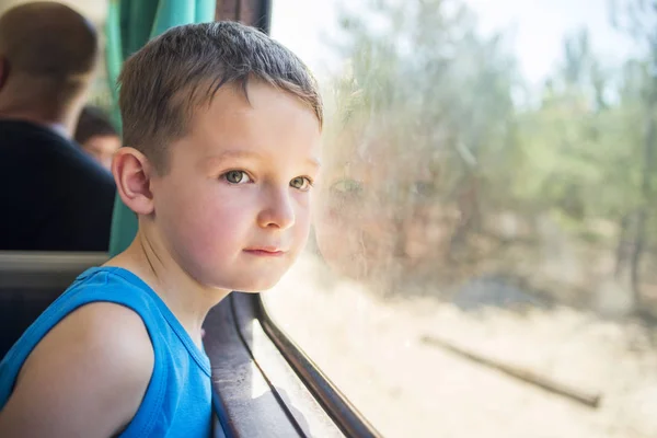 Chlapec cestuje vlakem a dívá se z okna, pozoruje pohybující se objekty za oknem. Chlapec ve vlaku u okna — Stock fotografie