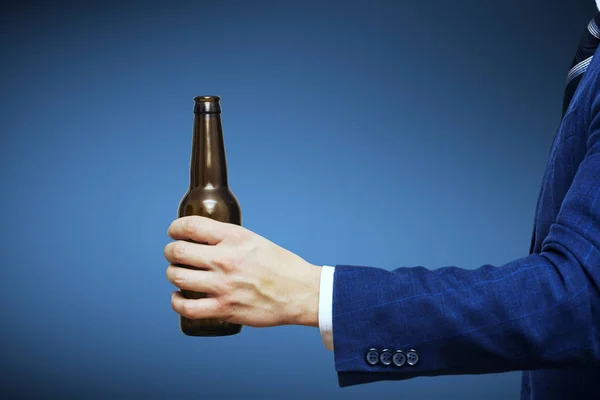 Uma mão de homem segurando garrafa de cerveja no fundo azul. Uma mão segurando uma garrafa de cerveja sem etiqueta — Fotografia de Stock