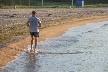 Tanınmayan adam boş tropik plajda koşuyor ve deniz suyuna sıçratıyor. Adam tropik sahilde koşuyor