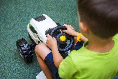 Küçük bir çocuk oyuncak bir traktör kullanıyor. Küçük çocuk beyaz oyuncak traktör kullanıyor.