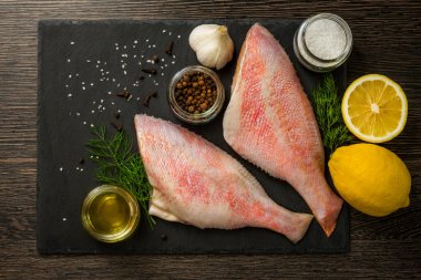 Kara tahtada deniz levreği. Deniz mi? İçinde pişirmek için gerekli malzemeler olan siyah bir tahtada levrek. Masada balık var. Okyanus levreği.