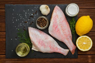 Deniz ürünleri. Kara tahtada deniz levreği. Kara tahtada kızıI deniz levreği. İçinde pişmesi için gerekli malzemeler var. Masada balık var. Okyanus levreği.