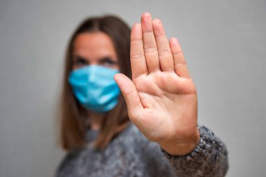 Yüzünde koruyucu maske takan kadın Coronavirus salgınını durdurmak için el hareketi yapıyor. Maskeli kadın elini uzatmaya odaklandı. Virüsü durdur..