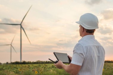 Mühendis rüzgar türbinindeki enerji üretimini kontrol ediyor. Yel değirmenindeki işçiler kaskla ve tabletle park ederler..