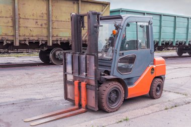 Forklift, açık bir deponun arazisindeki özel ekipman demiryolu yükleme istasyonundaki yük vagonlarının arka planına karşı..