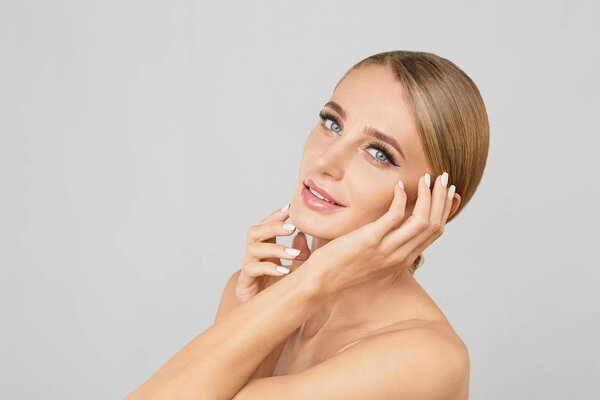 Portrait of smiling beautiful blonde woman with natural make up touching her face. Beauty young woman with fresh clean perfect skin. Skin care concept. Cosmetology,beauty and spa. Facial treatment.