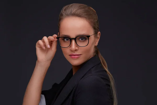 Elegant serious woman in square eyeglasses looking at camera on dark background.Adult beautiful businesswoman in jacket.Black frame spectacles.Vision correction,optical shop,glasses store concept.