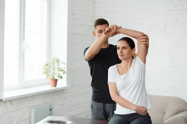 Female patient doing physical exercises with physiotherapist. Male therapist treating injured shoulder of young athlete. Post traumatic rehabilitation, sport physical therapy, recovery concept.