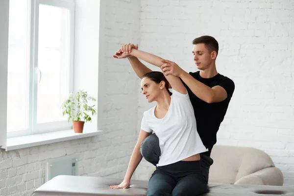 Female patient doing physical exercises with physiotherapist. Male therapist treating injured shoulder of young athlete. Post traumatic rehabilitation, sport physical therapy, recovery concept.