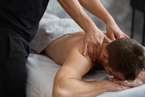 年轻英俊的男人享受背部按摩 专业的按摩治疗师正在公寓治疗一名男性病人 身体和面部治疗的概念 家庭按摩 — 图库照片