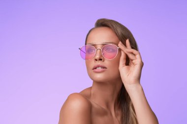 Pembe güneş gözlüğü giyen mükemmel makyaj ile güzel genç kadının portresi. Lila arka planda poz Aviator Güneş gözlüğü gülümseyen moda modeli. Stüdyo çekimi. Yaz tatili.