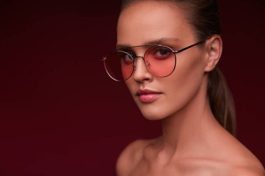 Pembe güneş gözlüğü giyen mükemmel makyaj ile güzel genç kadının portresi. Bordo arka planda poz Aviator Güneş gözlüğü gülümseyen moda modeli. Stüdyo çekimi. Yaz tatili.