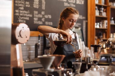 Kahve makinesi ve su ısıtıcısının üzerine dökülen kimyasallarla kahve hazırlayan profesyonel barista. Kahve yapan genç bir kadın. Kahve demlemenin alternatif yolları. Kahve dükkanı konsepti.