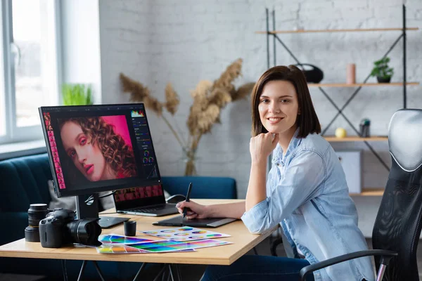 Portrait of graphic designer working in office with laptop,monitor,graphic drawing tablet and color palette.Retouching images in special program.Retoucher workplace in photo studio.Creative agency
