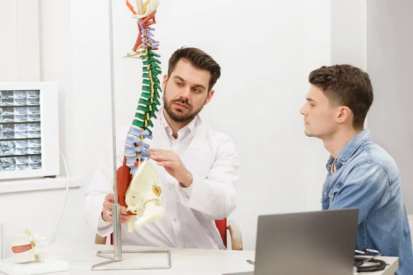 Docteur montrant le modèle flexible de colonne vertébrale à son patient et explique la cause de sa douleur au cabinet médical. Le patient rend visite à un physiothérapeute en clinique. Chirurgie, santé et médecine concept — Photo