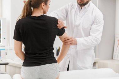 Erkek doktor, dirsek ağrısı çeken kadın hastayı muayene ediyor. Tıbbi muayene. Kayropraktik, osteopati, travma sonrası rehabilitasyon, spor fizyoterapisi. Alternatif tıp, ağrı kesici kavramı