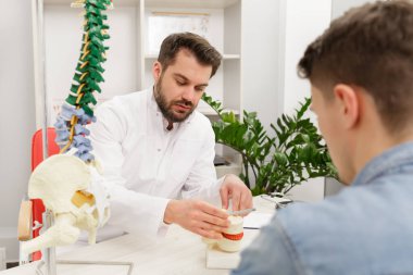 Doktor, hastasına esnek omurga modeli gösteriyor ve muayenehanedeki ağrısının nedenini açıklıyor. Klinikteki fizyoterapisti ziyaret eden hasta. Cerrahi, sağlık ve tıp konsepti