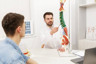 Doktor, hastasına esnek omurga modeli gösteriyor ve muayenehanedeki ağrısının nedenini açıklıyor. Klinikteki fizyoterapisti ziyaret eden hasta. Cerrahi, sağlık ve tıp konsepti