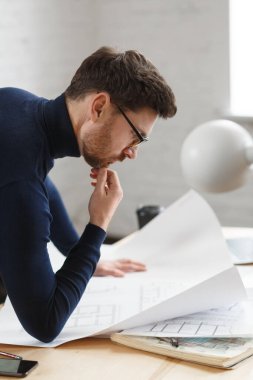 Ofiste planlarla çalışan bir mimar. Mühendis mimari planı inceliyor, bir inşaat projesi çiziyor. İş yerinde oturan sakallı yakışıklı bir adamın portresi. İş inşa kavramı
