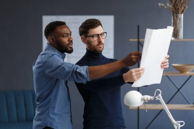 Çok ırklı mühendis ekibi mavi baskılar ve mimar ekipmanlarıyla birlikte çalışıyor, taslak çiziyorlar, tartışıyorlar ve inşaat projesini planlıyorlar. Ortaklar iş yerinde tartışır. İş inşa kavramı