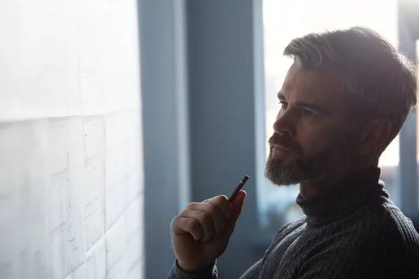 Retrato de cerca del hombre guapo concentrado en el trabajo. Arquitecto trabajando en oficina con planos. Ingeniero dibujando un proyecto de construcción. Plano arquitectónico. Concepto de construcción empresarial —  Fotos de Stock