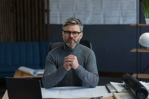 Üzleti portré egy jóképű szakállas férfiról, aki szemüvegben ül a munkahelyén. A magabiztos üzletember sikeres lett. Belsőépítész, aki laptoppal dolgozik. Üzleti koncepció — Stock Fotó