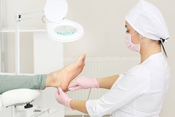 Peeling feet with special electric device.Professional hardware pedicure using electric machine.Patient on medical pedicure procedure, visiting podiatrist.Foot treatment in SPA salon.Podiatry clinic