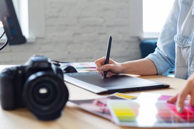 Grafik tasarımcı ellerinin özel programda grafik çizim tableti kullanarak resimleri rötuşladığı portreyi kapat. Laptop, monitör ve renk paleti. Fotoğraf stüdyosundaki işyerinde. Yaratıcı ajans